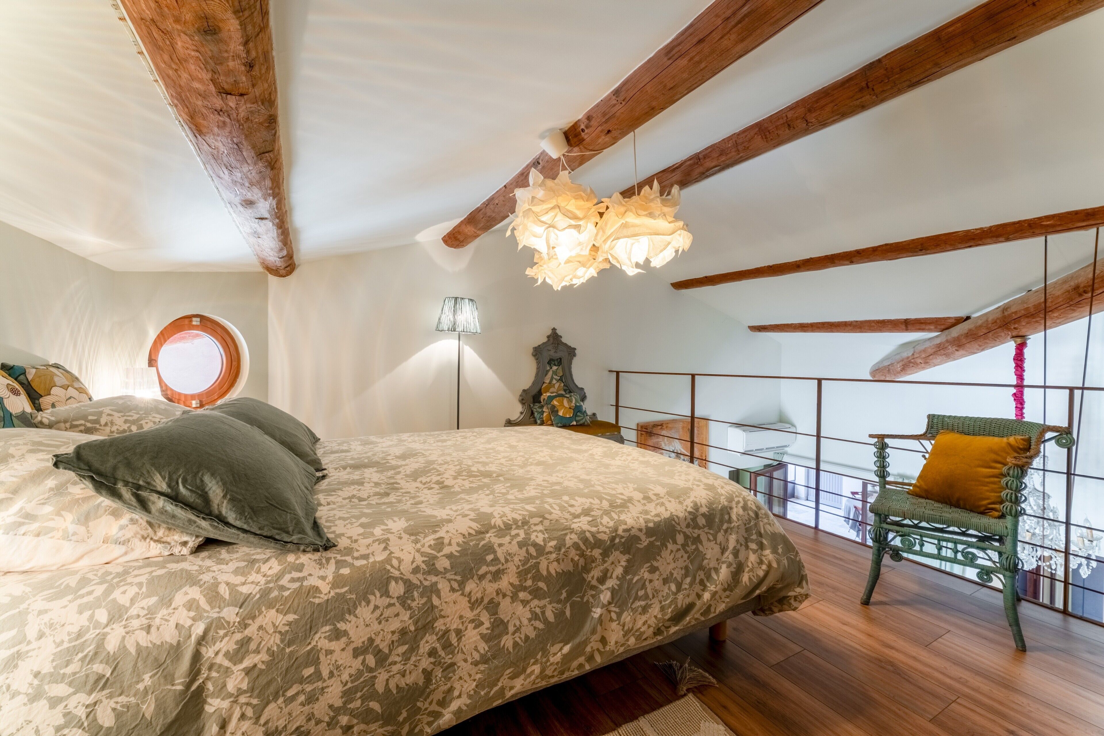 Ein Schlafzimmer mit Bett, Stuhl, Lampe und einem Balkon mit Blick.