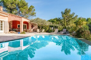 Une piscine avec des chaises longues, un patio couvert et un bâtiment aux murs rouges.