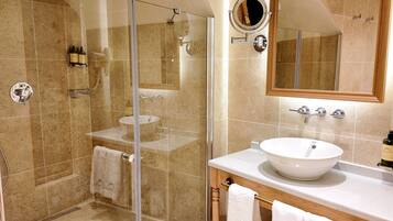 Un baño con ducha de vidrio, un lavamanos con un espejo grande y un tocador con toallas.