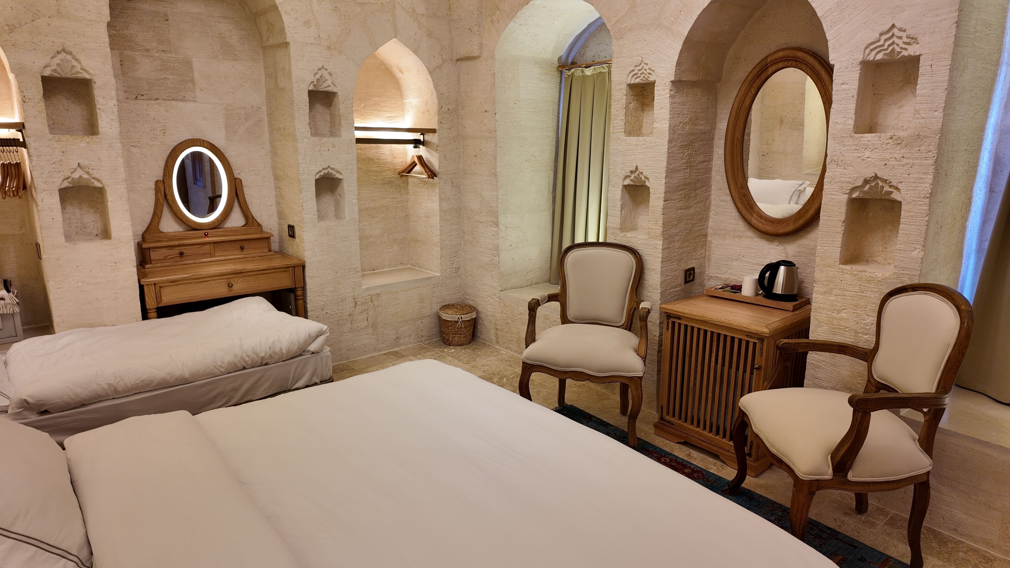 A hotel room with two beds, a wooden dresser, a mirror, and a small table with a kettle.