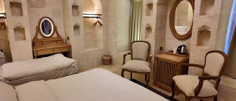 A hotel room with two beds, a wooden dresser, a mirror, and a small table with a kettle.