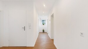 A hallway with wooden flooring, white walls, and a window at the end. - Apartment '2' with Shared Garden, Balcony, and Wi-Fi (Bad Dürrheim)