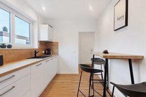 Eine moderne Küche mit weißen Schränken, einer Holzausziehtafel, einem schwarzen Spülbecken und einem Fenster mit Blumentöpfen.