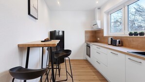 A modern kitchen with a wooden table, black chairs, a black refrigerator, and a window with potted plants. - Apartment '2' with Shared Garden, Balcony, and Wi-Fi (Bad Dürrheim)