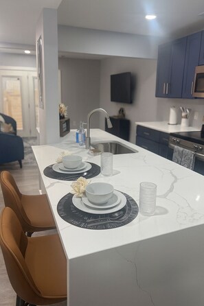 A modern kitchen with a white marble island, stainless steel appliances, and a flat-screen TV mounted above the counter. - Walk to Mass Ave - Near Lucas Oil - Free Parking (Indianapolis)