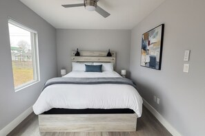 Une chambre à coucher avec un lit, un ventilateur de plafond, une fenêtre et un tableau accroché au mur.