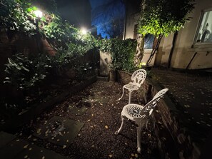 Ein Sitzbereich im Freien mit zwei weißen Stühlen, einer Ziegelwand und einem Blumentopf.