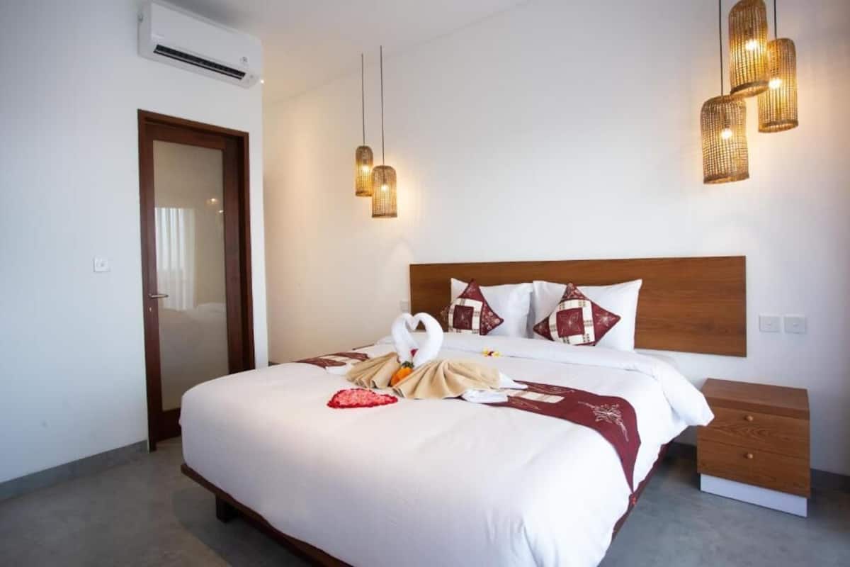 Ein Hotelzimmer mit einem großen Bett, einem Holzkopfteil, einem Nachttisch und einer Wand-Klimaanlage.