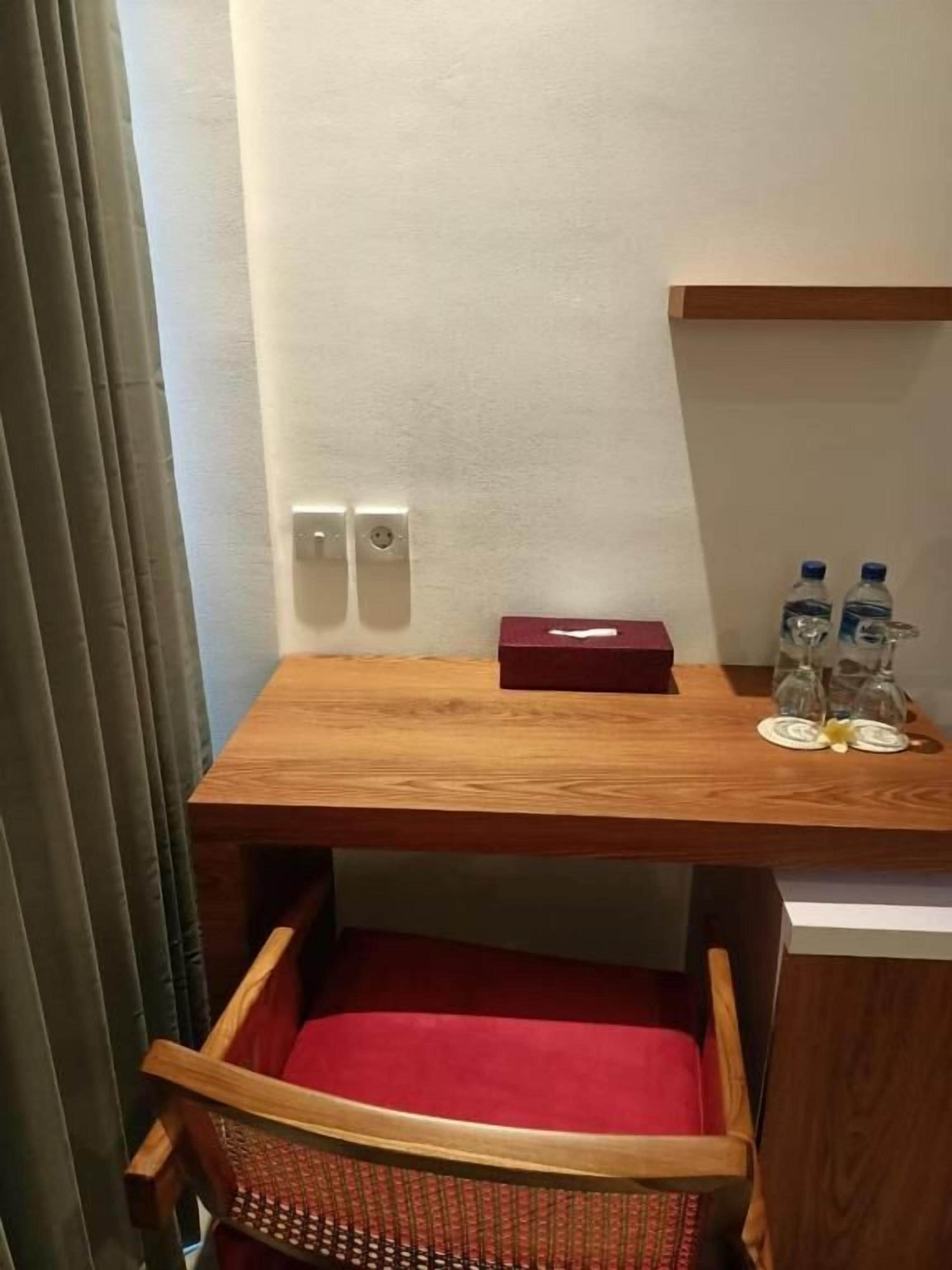 Uma pequena mesa de madeira com um encosto vermelho, uma caixa vermelha e duas garrafas de água sobre uma prateleira fixada na parede.