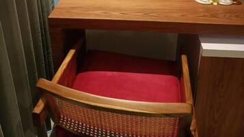 Uma pequena mesa de madeira com um encosto vermelho, uma caixa vermelha e duas garrafas de água sobre uma prateleira fixada na parede.