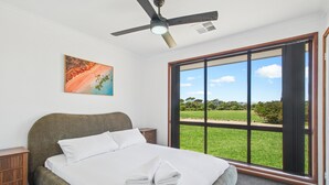 A bedroom with a bed, a ceiling fan, a window with a view of a green landscape, and a painting on the wall. - Seabreeze Acres ~ Maslin Beach - Seabreeze Acres = Coastal Serenity! (Maslin Beach)