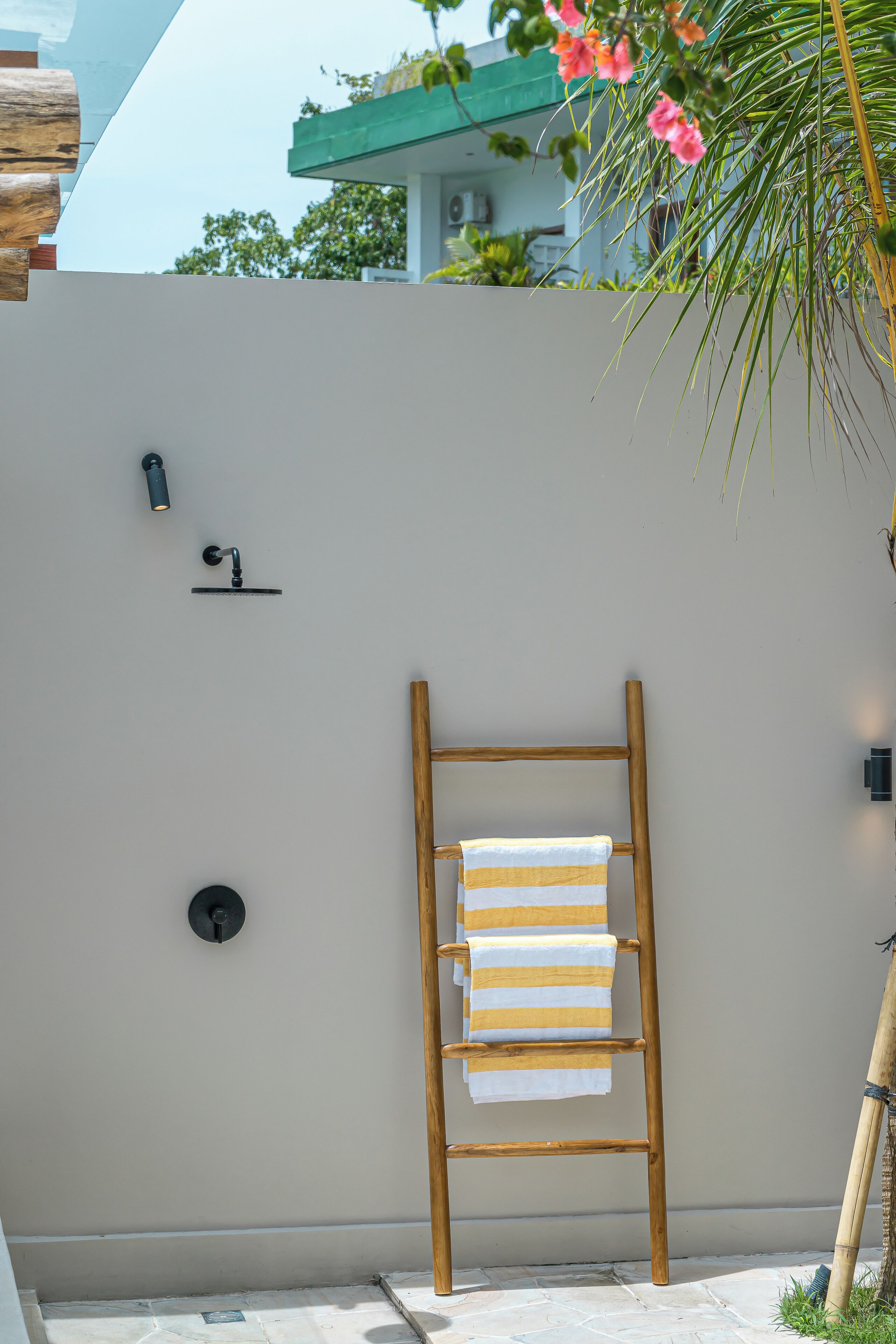 Un baño exterior moderno con una escalera de madera, un perchero y un cabezal de ducha empotrado.
