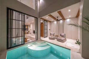 Un intérieur moderne avec une piscine, un espace salon et un escalier menant à un balcon.