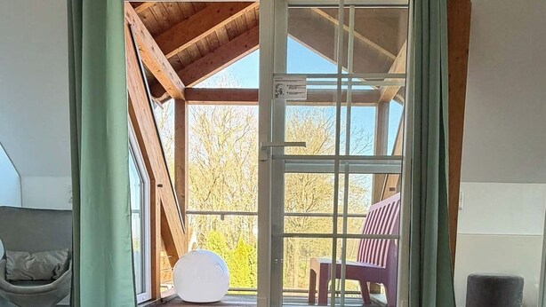 Una habitación con un amplio ventanal corredera que da a un balcón, una alfombra colorida y una silla.