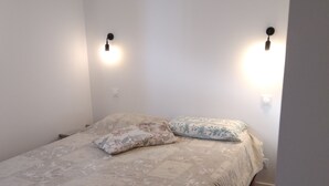 Ett litet, välordnat sovrum med en säng, två vägglampor och en luftkonditioneringsanläggning.