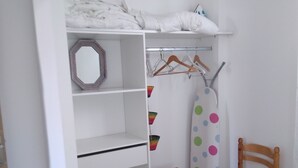 Ett litet rum med en vit garderob, en trästol och en färgglad strykbräda.