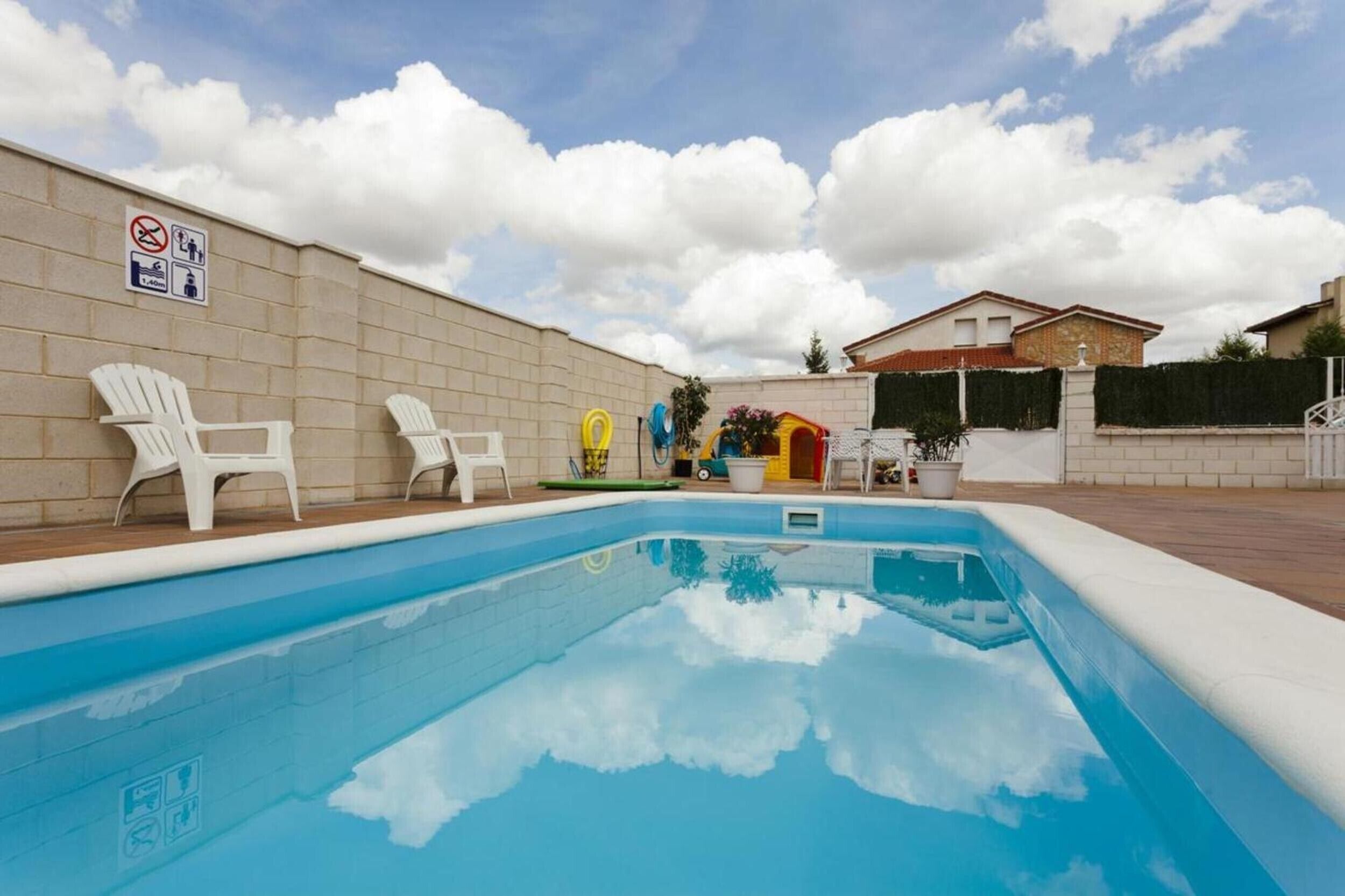 Una piscina con sillas de descanso blancas, un letrero de prohibición de bañarse y un muro de ladrillo.