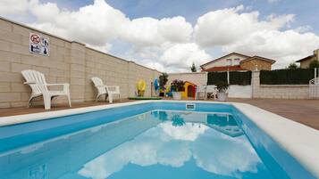 Una piscina con sillas de descanso blancas, un letrero de prohibición de bañarse y un muro de ladrillo.