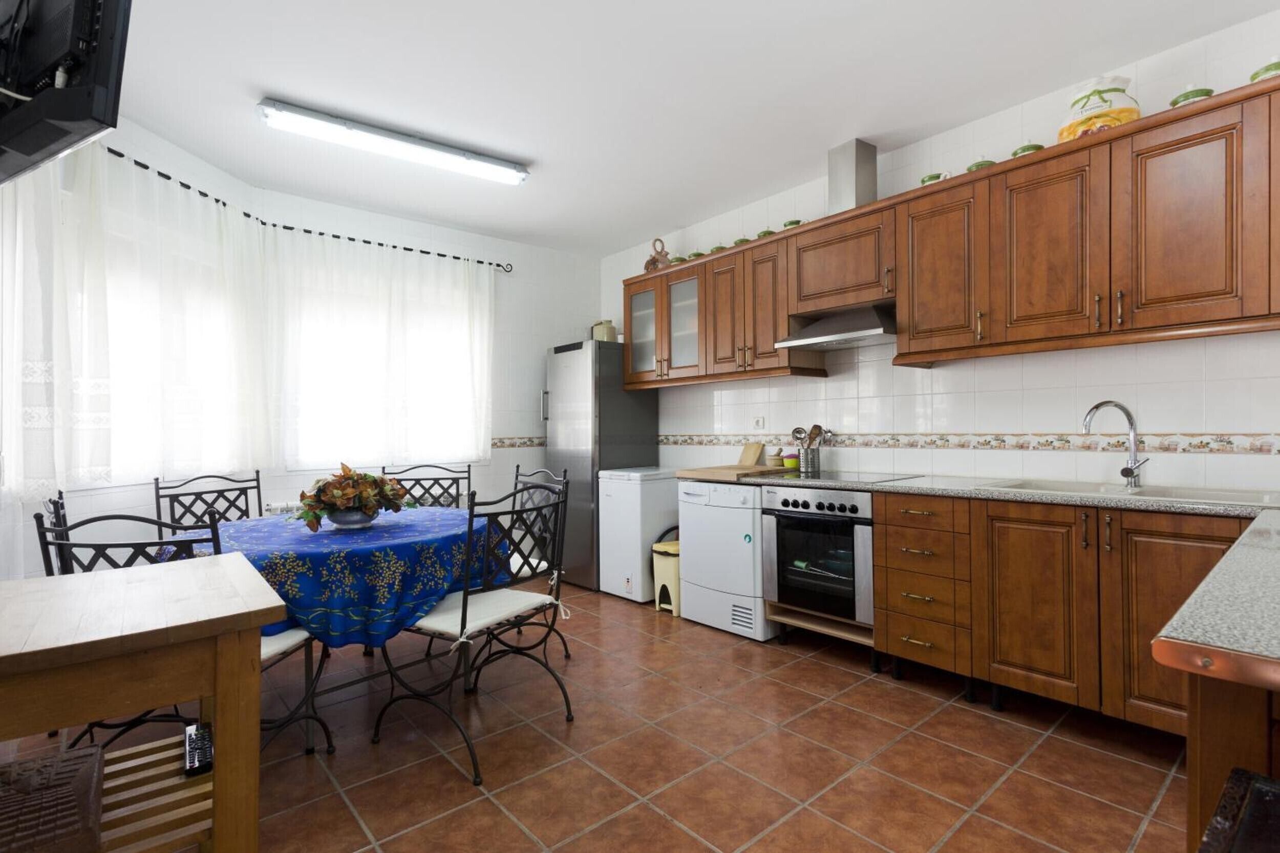 A kitchen with wooden cabinets, a dining table with chairs, a refrigerator, a stove, and a sink.