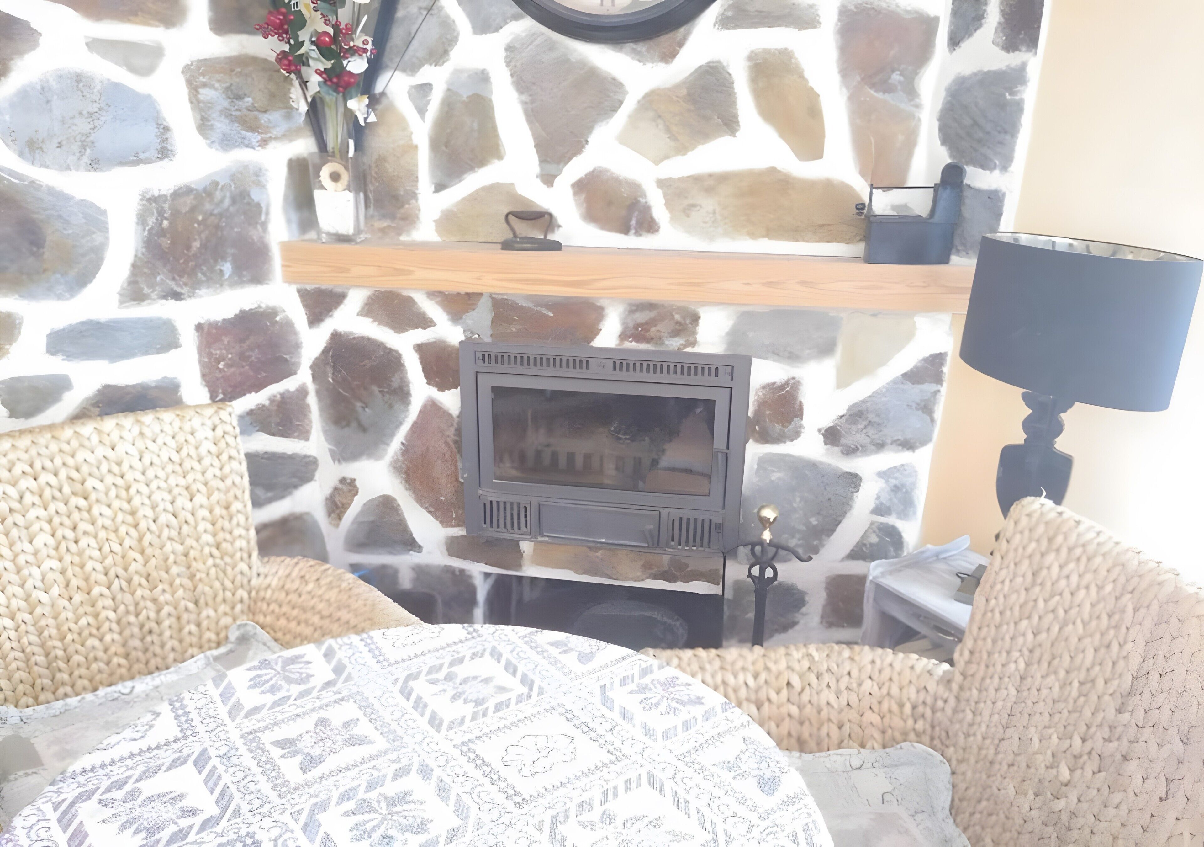 Eine Steinsäule mit Kamin, einem Holzregal und einer Lampe.