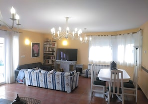 A living room with a sofa, TV, bookshelf, dining table, and chandelier.