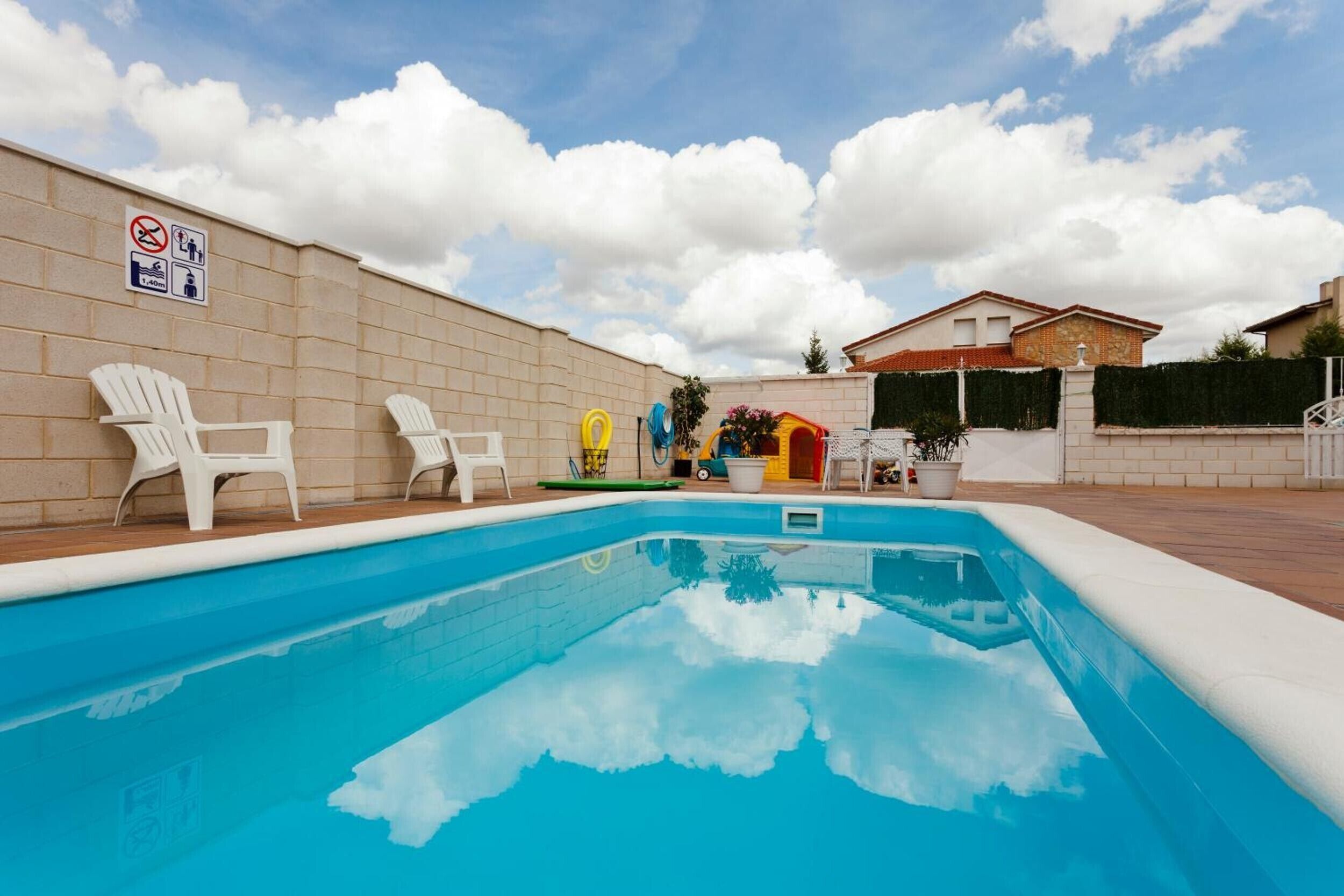 Una piscina con sillas blancas, un letrero que indica que no se permite nadar y un edificio al fondo.