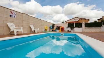 Una piscina con sillas blancas, un letrero que indica que no se permite nadar y un edificio al fondo.