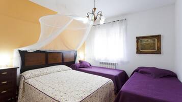 Una camera da letto con un letto, due comodini, un tavolino, una sedia, una finestra con tende leggere, un lampadario e un quadro appeso al muro.