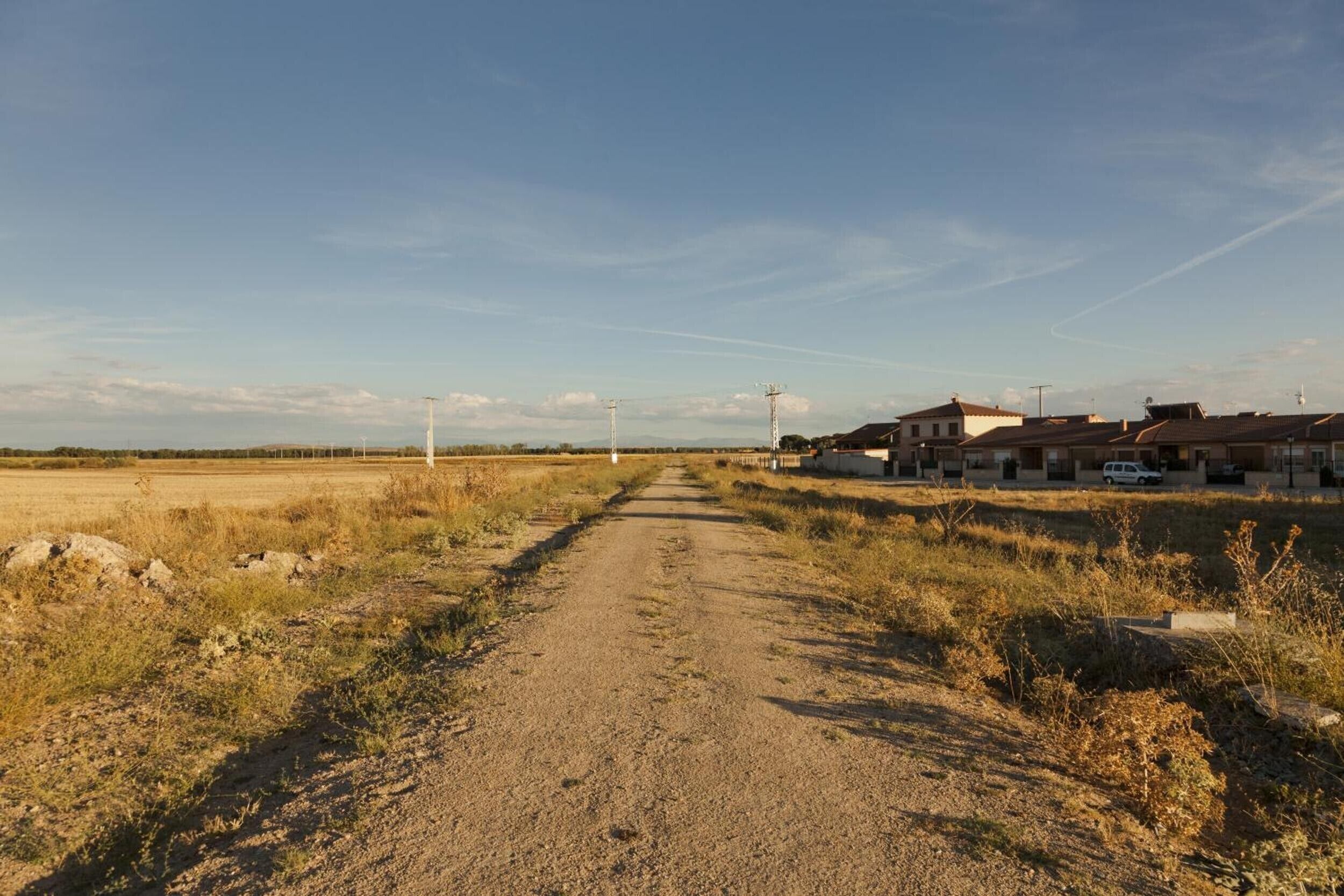 A rural road leading to a row of houses with a clear sky.