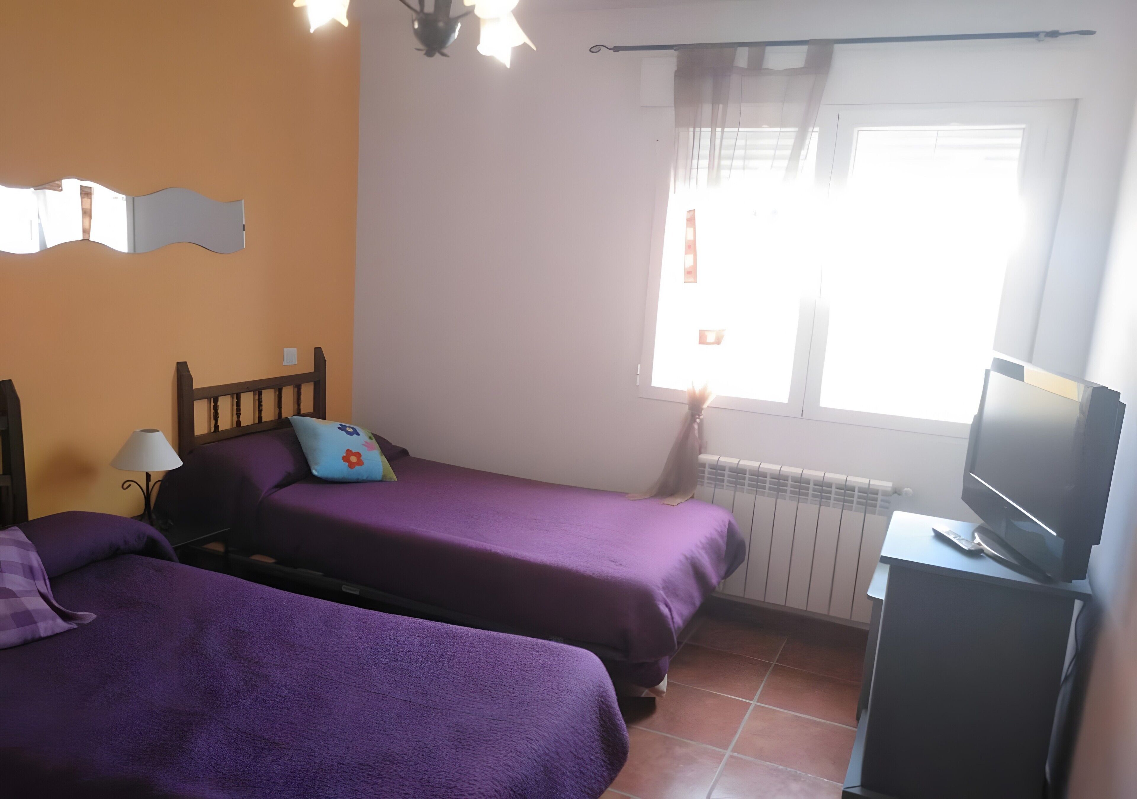 Una habitación con dos camas, televisión, ventana con cortinas y radiador.
