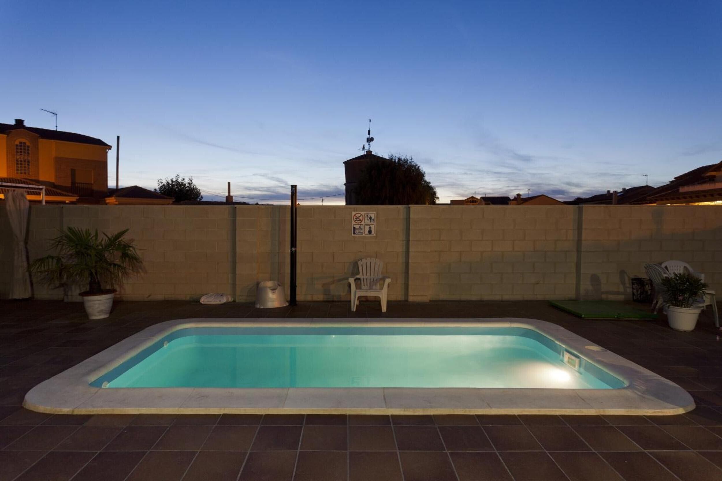 A rectangular swimming pool with a tiled deck, a brick wall, and a chair.