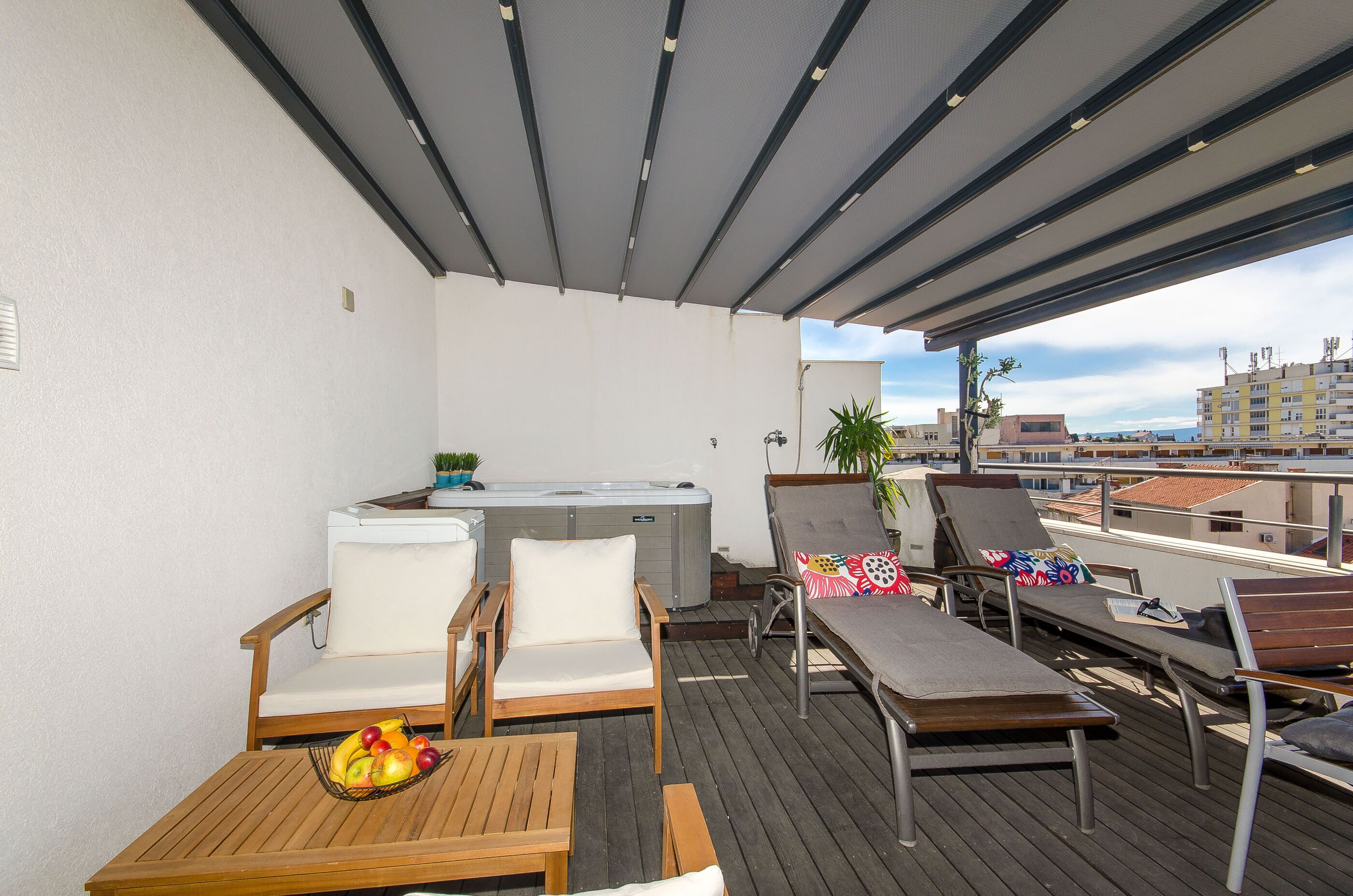 A rooftop terrace with wooden furniture, a hot tub, and a view of the cityscape.
