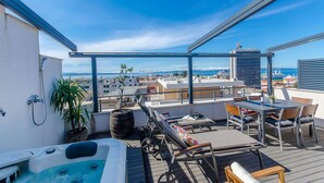 Eine Dachterrasse mit Whirlpool, Liegestühlen und einem Tisch mit Stühlen.