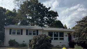 A single-story house with a front yard, a small bush, and a tree in the background. - Charming Raleigh Retreat (Raleigh)