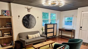 A living room with a sofa, two armchairs, a coffee table, a bookshelf, a decorative wall piece, a cabinet, and a window with a view of trees. - Charming Raleigh Retreat (Raleigh)