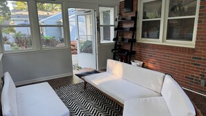A cozy room with a white sofa, a small table, and a black and white patterned rug. A brick wall and a window with a view of the outside are visible. - Charming Raleigh Retreat (Raleigh)