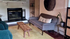 A modern living room with a fireplace, a grey sofa, a blue armchair, and a wooden coffee table. - Charming Raleigh Retreat (Raleigh)