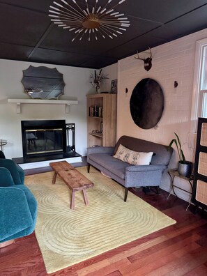 A modern living room with a fireplace, a grey sofa, a blue armchair, and a wooden coffee table. - Charming Raleigh Retreat (Raleigh)