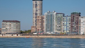Paisagem costeira com edifícios modernos altos, uma praia de areia e águas calmas.