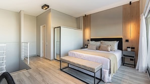 Quarto moderno com cama grande, um banquinho, uma escrivaninha e um espelho.