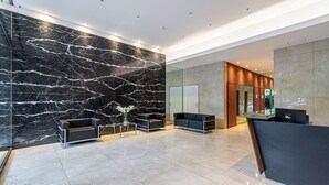 Uma área de recepção moderna com paredes de mármore, divisória de vidro e balcão de atendimento.