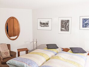 Ein Schlafzimmer mit einem Bett, einem Sessel, einem Spiegel und drei gerahmten Bildern an der Wand.