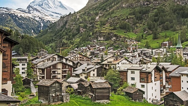 Un pueblo montañoso con casas de madera tradicionales, una iglesia y un pico de montaña destacado al fondo.