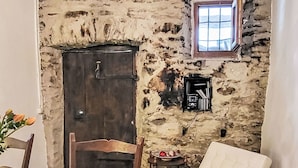A rustic stone wall with a wooden door, a small window, and a cozy seating area with a white cushion and a white fluffy object. - Wonderful private villa for 4 people with patio and pets allowed (Someo)