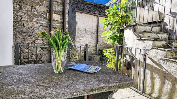 A stone table with a vase of flowers and a book, set against a stone wall with a mountain view. - Wonderful private villa for 4 people with patio and pets allowed (Someo)