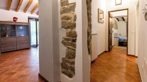 Ein Korridor mit Steinwand, Holzbalken, Fliesenboden und einem Bett im angrenzenden Zimmer.