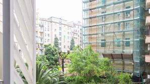Une vue depuis un balcon donnant sur un paysage urbain, avec des immeubles de plusieurs étages, dont certains sont en construction et sont entourés d’échafaudages, et de luxuriants arbres verdoyants.