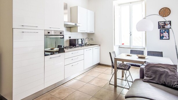 Une cuisine moderne avec des meubles blancs, un coin repas comprenant une table et des chaises, et un canapé dans l’espace salon.