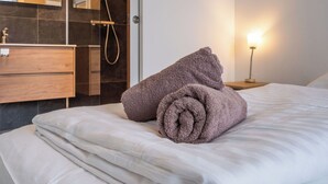 Habitación de hotel con cama, mesita de noche con lámpara, baño con espejo y una toalla sobre la cama.