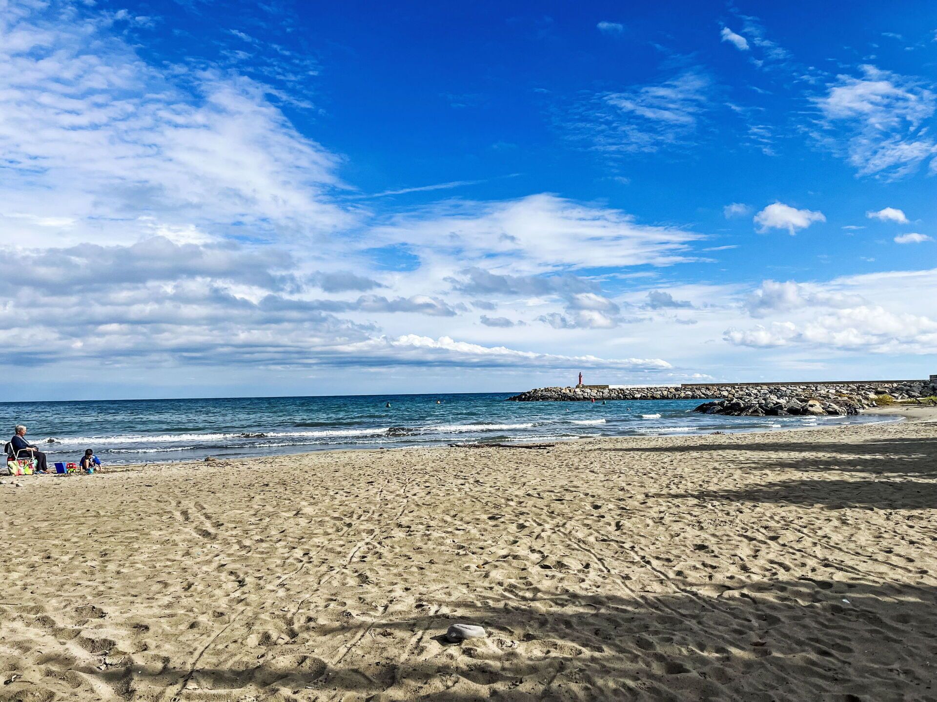 En sandstrand med fodspor, en klippefyldt bøde og en klar blå himmel.